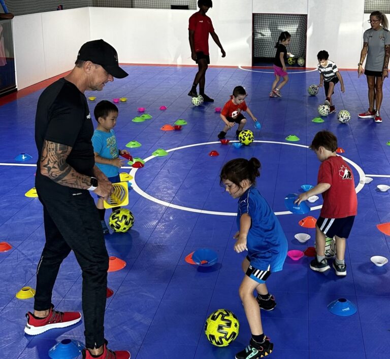 Kids playing indoor soccer with their coach.