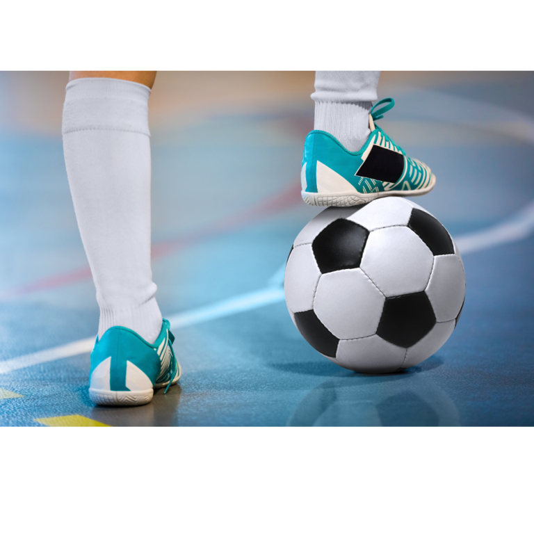 A kid has one foot on a soccer ball and the other on an indoor soccer court.